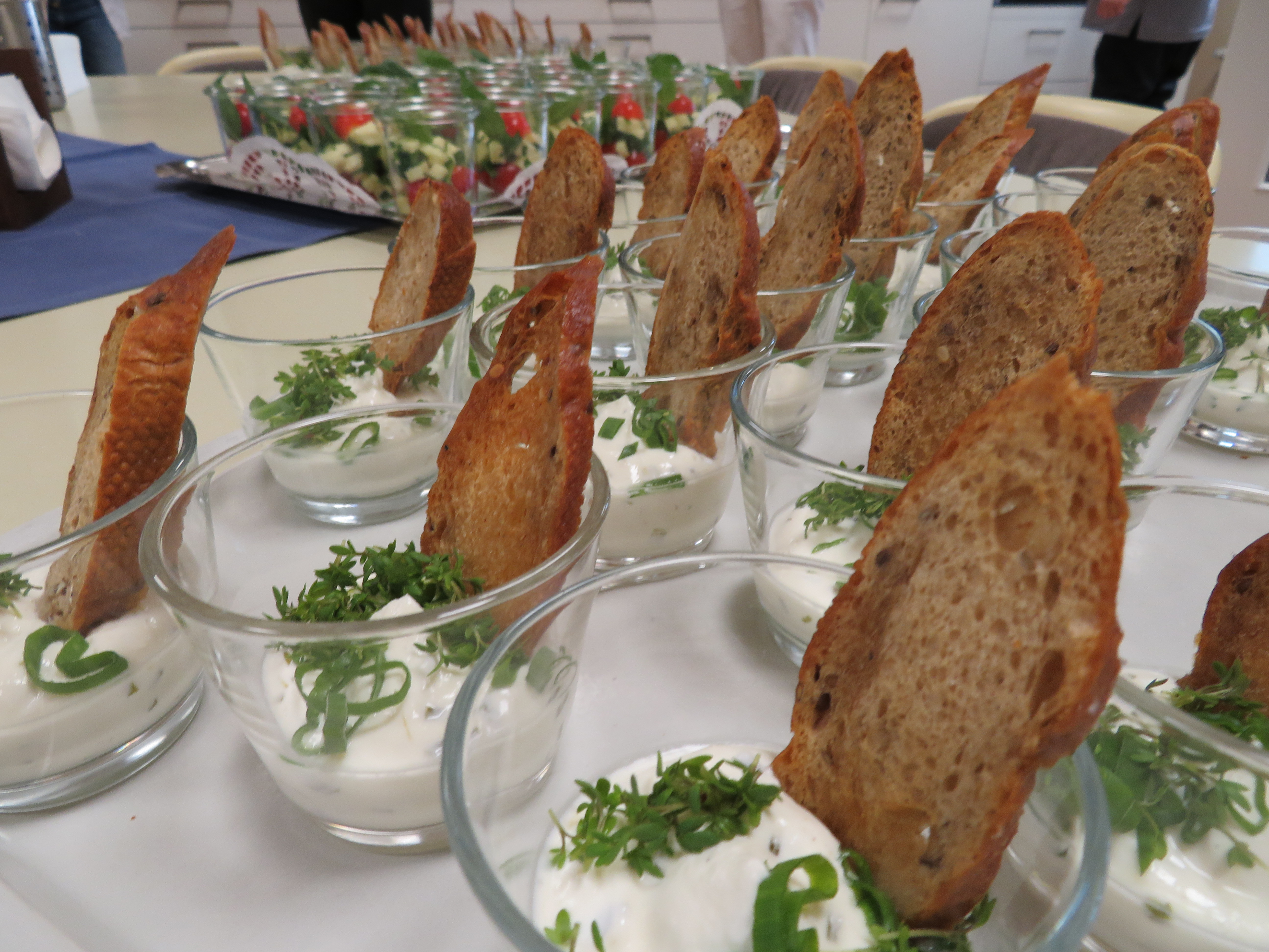 Gläser mit Joghurt, garniert mit Kräutern und knusprigem Brot.